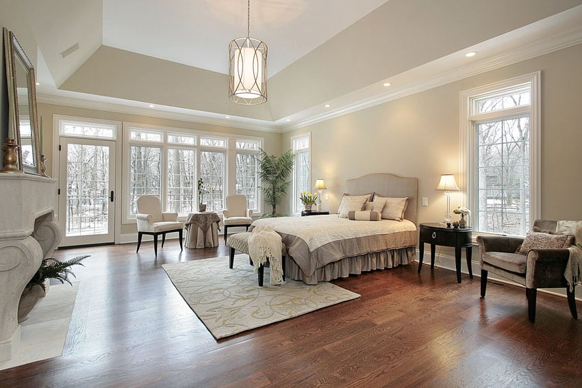 bedroom in new construction home with tray inclined ceiling, wood grain floors and fireplace