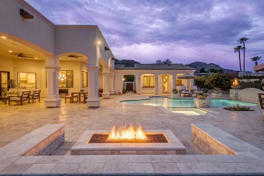Luxury patio with stone bench seating around fire pit with pool views