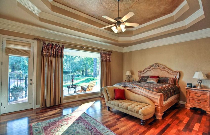 bedroom with tray tiered ceiling, wood stained floors and large picture window with door to patio