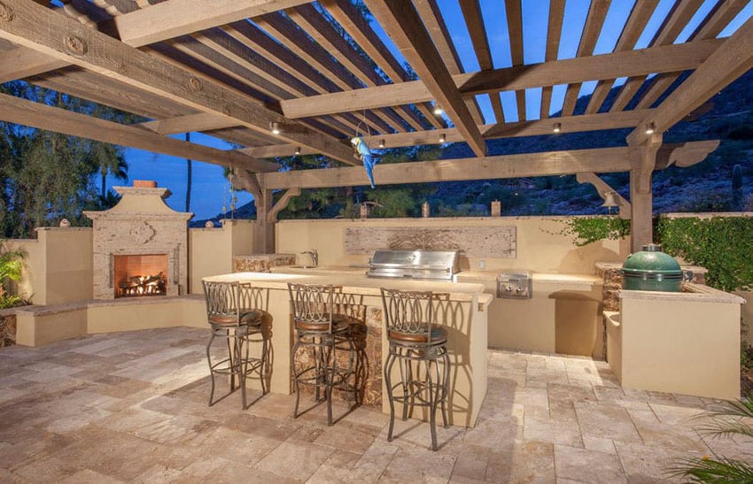 Patio with wood pergola with a fireplace in a corner and counters with chairs