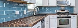 small-l-shaped-kitchen-with-white-cabinets-blue-subway-tile-and-wood-countertops