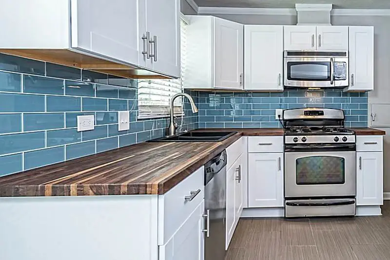 Small l shaped kitchen with white cabinets blue subway tile and wood countertops
