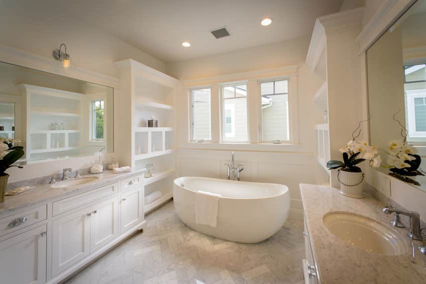 Traditional master bathroom with soaking bathtub and white vanities with marble counters