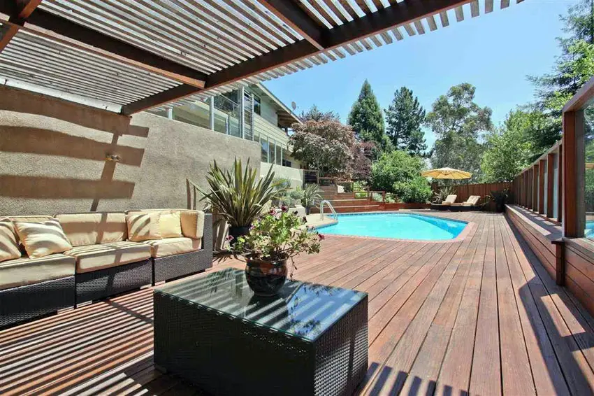 Wood deck surrounding swimming pool with pergola