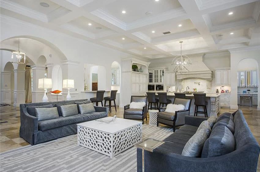 beautiful living room with box beam coffered ceiling and gray couches and chairs open to kitchen