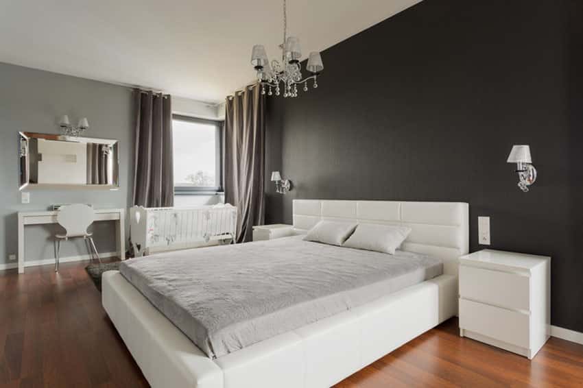 Bedroom with solid black walls white bed chandelier and wood floors