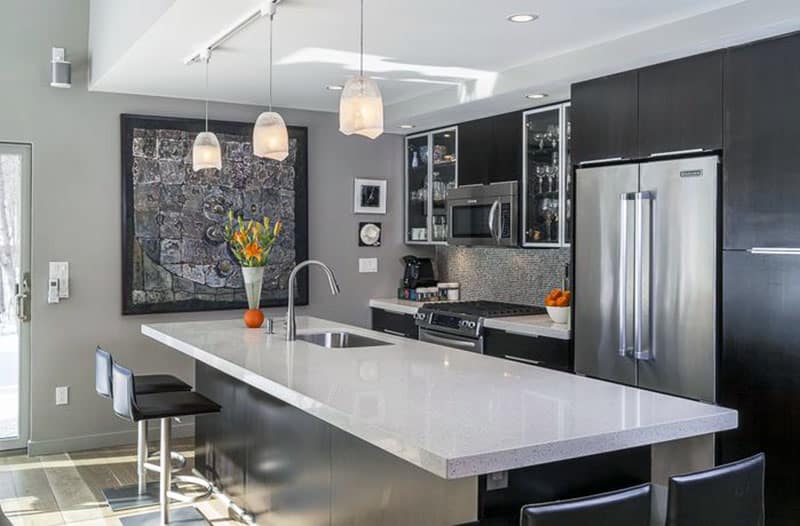 Dark cabinet kitchen with white quartz counter natural stone mosaic tile backsplash and pendant lights