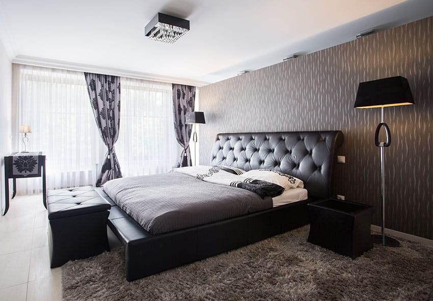 Dark themed bedroom with black leather bed frame and headboard with ottoman