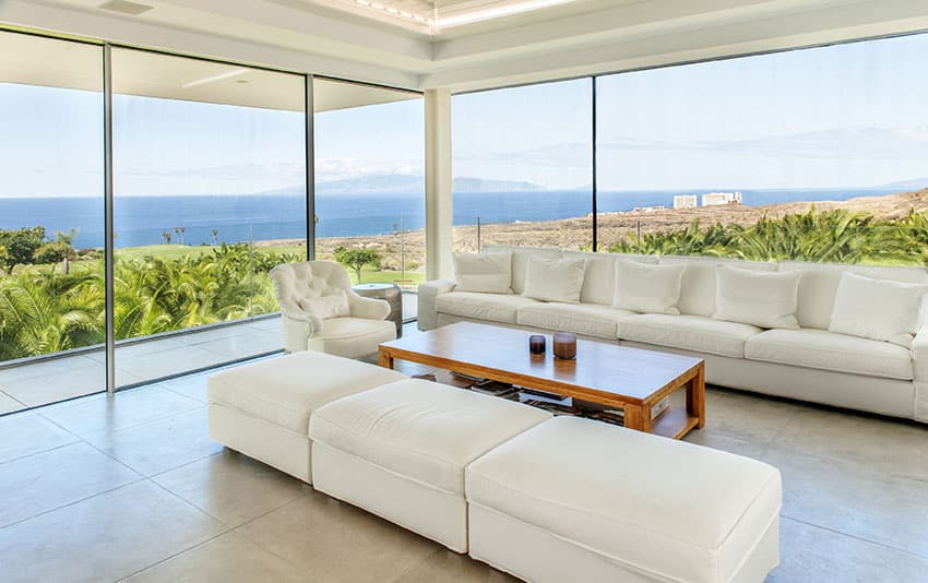 Gorgeous ocean view living room with wraparound windows and white furniture