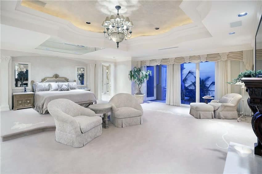 Luxury bedroom with elevated bed platform tray ceiling chandelier and balcony