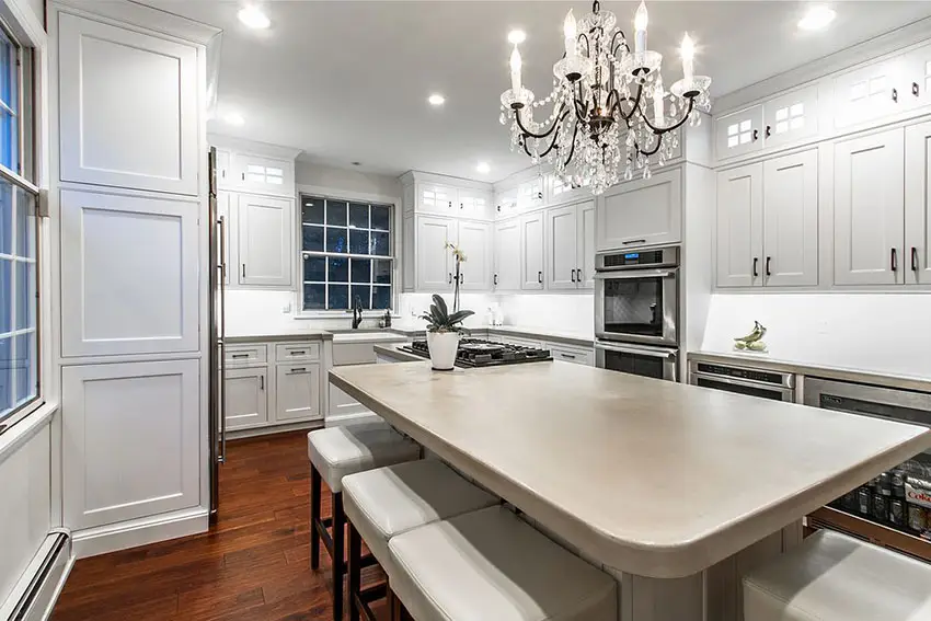 Luxury kitchen with concrete counter island with breakfast bar, chandelier and white cabinetry