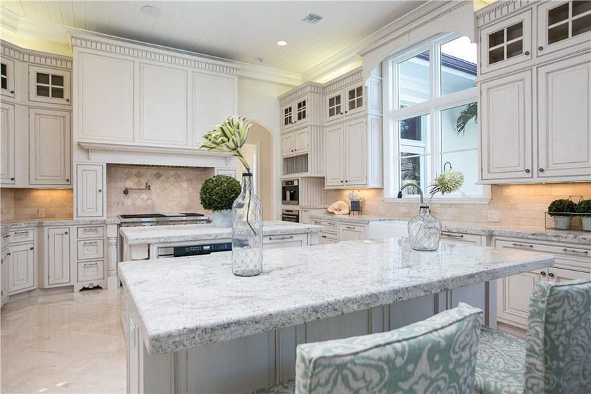 Luxury kitchen with white cabinetry, giallo fantasia granite counter, center island, dining island and marble floors