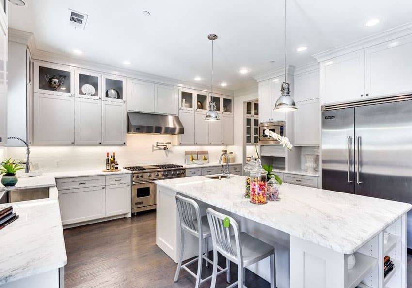 Luxury kitchen with white cabinetry, large marble topped island with vintage pendant lighting and wood floors