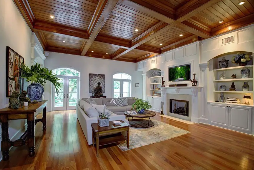 Luxury living room with large l shape sectional sofa wood floors wood beam ceiling and built in bookcase with fireplace