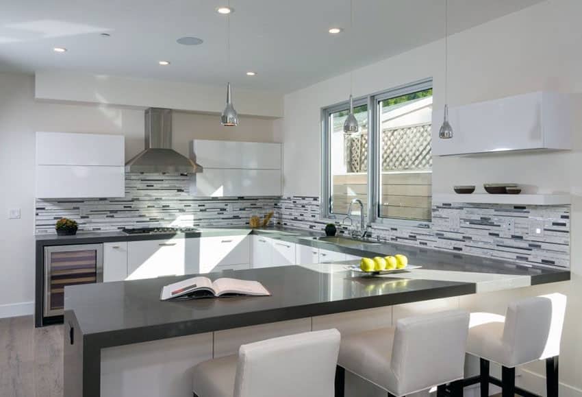 Modern u shaped kitchen with gray quartz counter, mosaic tile backsplash, pendant lights and armless stools