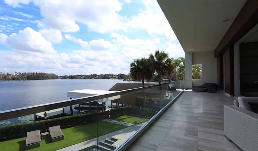 Top floor patio view of lake from modern home with glass railings and outdoor chairs