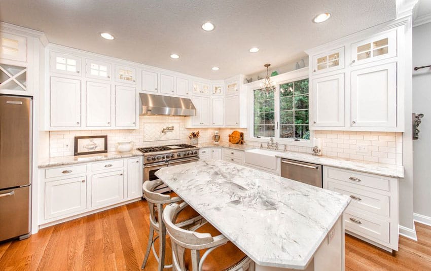 Traditional kitchen with marble counter island and white cabinets with glass pane windows