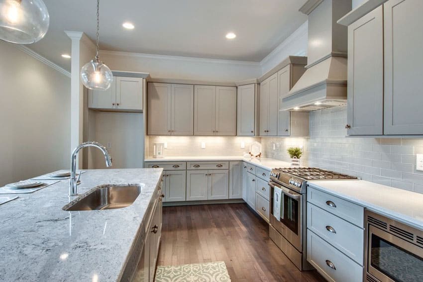 Transitional kitchen with gray cabinets, arctic white quartz, snowfall granite countertops, subway tile and globe pendant lights