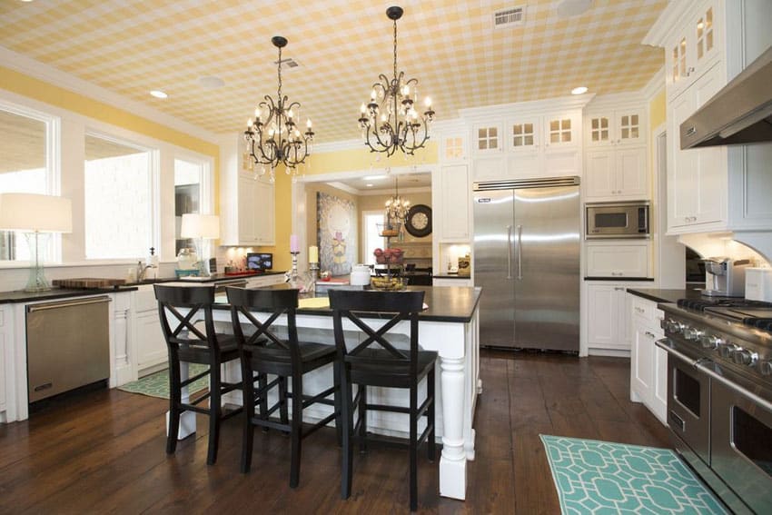 White country kitchen with yellow painted walls, chandeliers, and black countertops