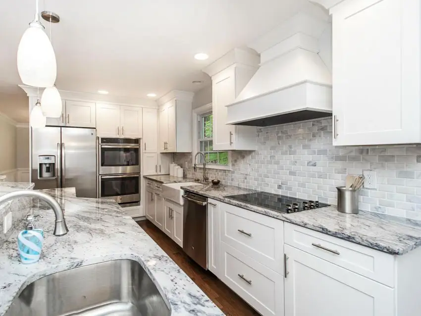 White cabinet kitchen with marble countertops and marble tile backsplash with mini pendant lighting
