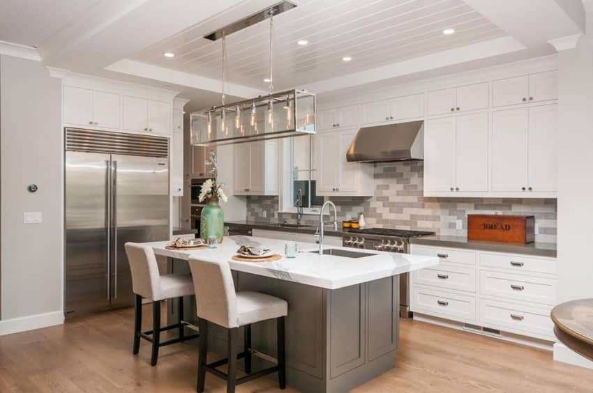 White transitional kitchen with dark color island with breakfast bar and marble counters