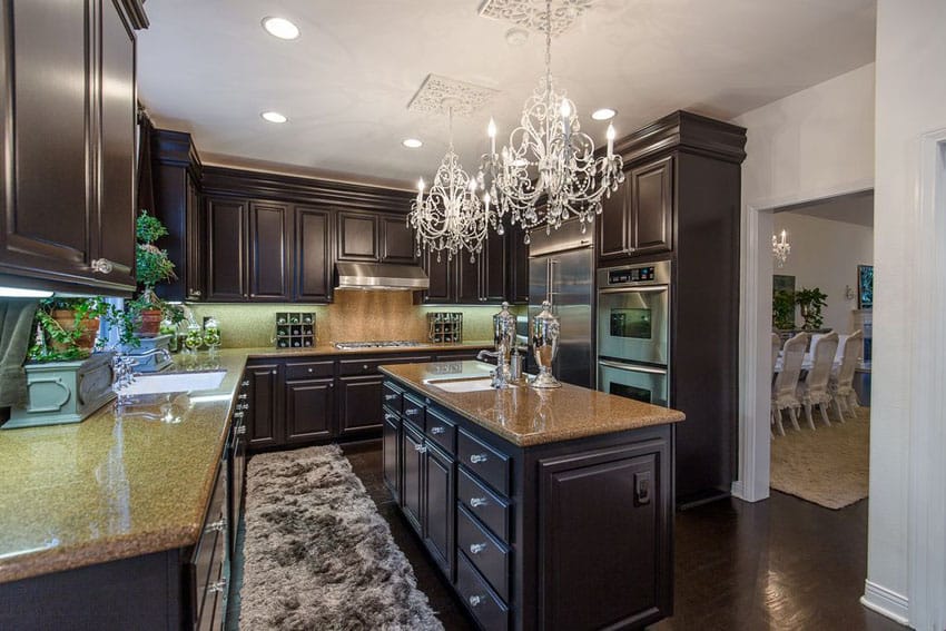 Dark cabinet traditional kitchen with beige granite counters and two chandeliers
