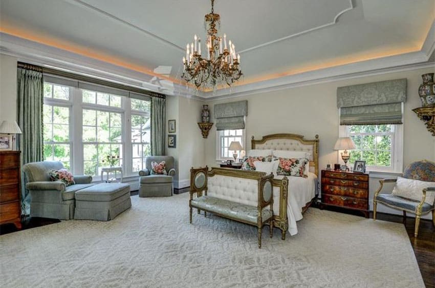 French provincial bedroom with tufted bed, chandelier, lounge chair, tray ceiling and vintage furniture