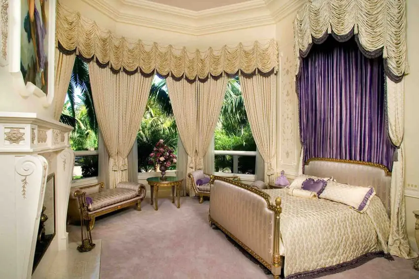 Gorgeous bedroom with gilded gold bed, bed drapery, large windows, gold furniture pieces and fireplace