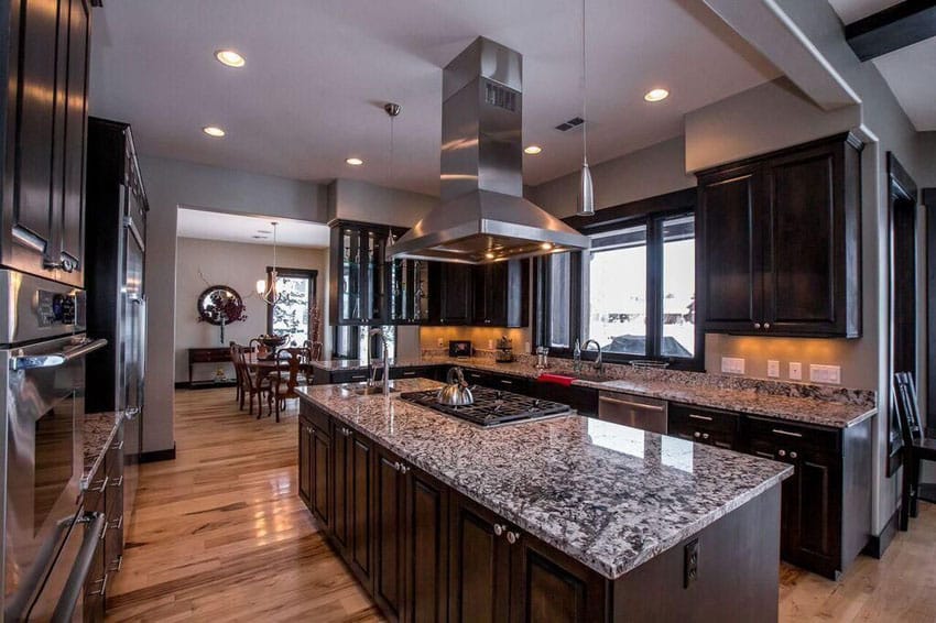 Kitchen with dark raised panel cabinets, center island with range and white wave granite counter