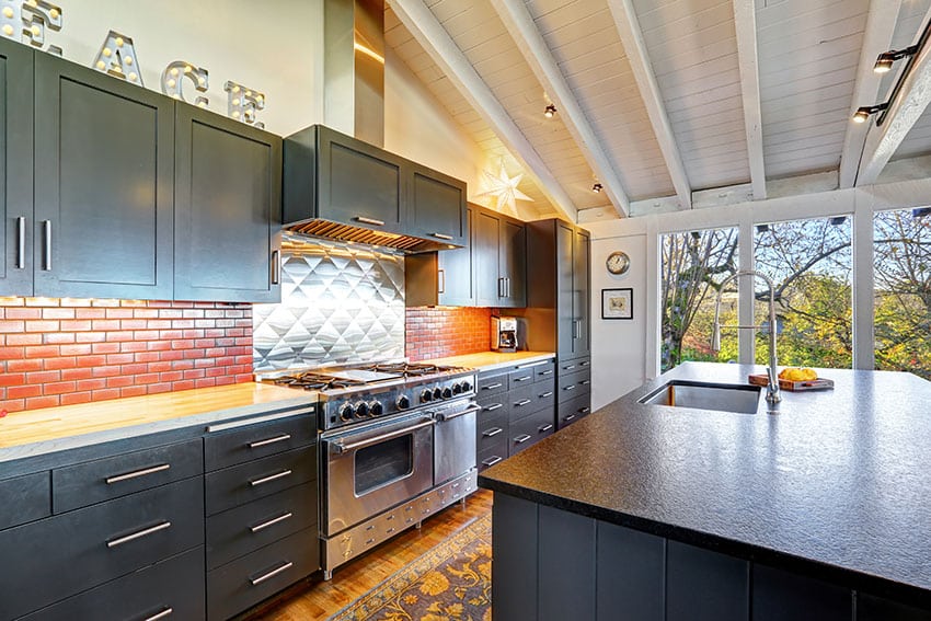 Modern kitchen with black cabinets, small brick backsplash, vaulted wood ceiling, and butcher block counter