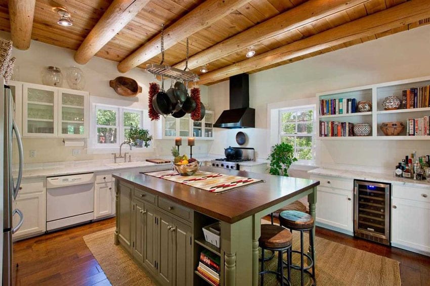 Kitchen with rustic wood countertop on green cabinet island, white cabinets and large round exposed beam ceiling