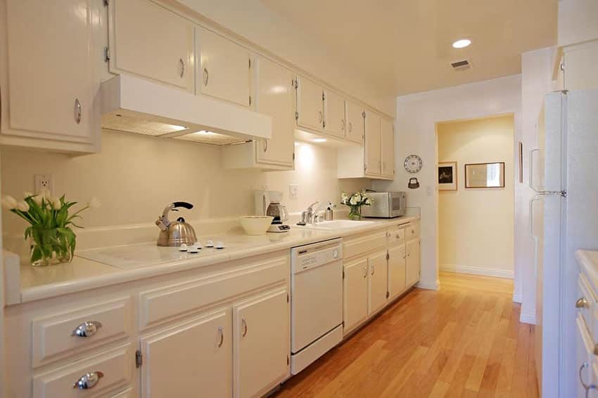 Traditional single line kitchen with corian solid surface counter, white cabinets and pecan engineered wood floors