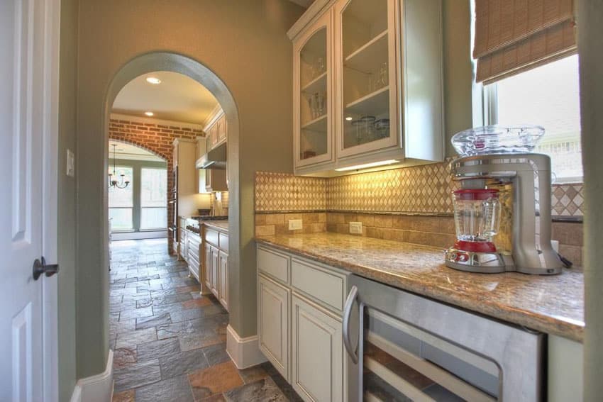 Traditional single wall kitchen with glass door, white cabinets and stone floors