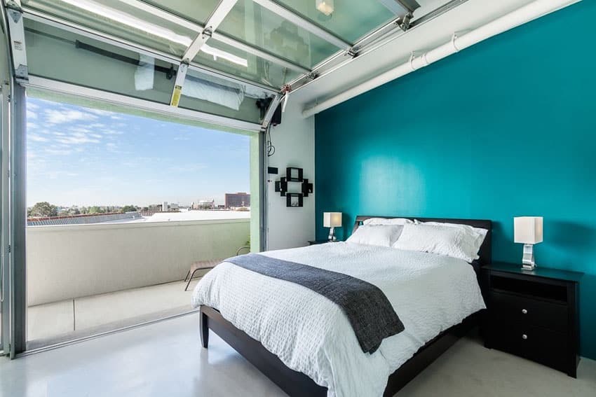 Bedroom with roll up door, teal wall, balcony and city views