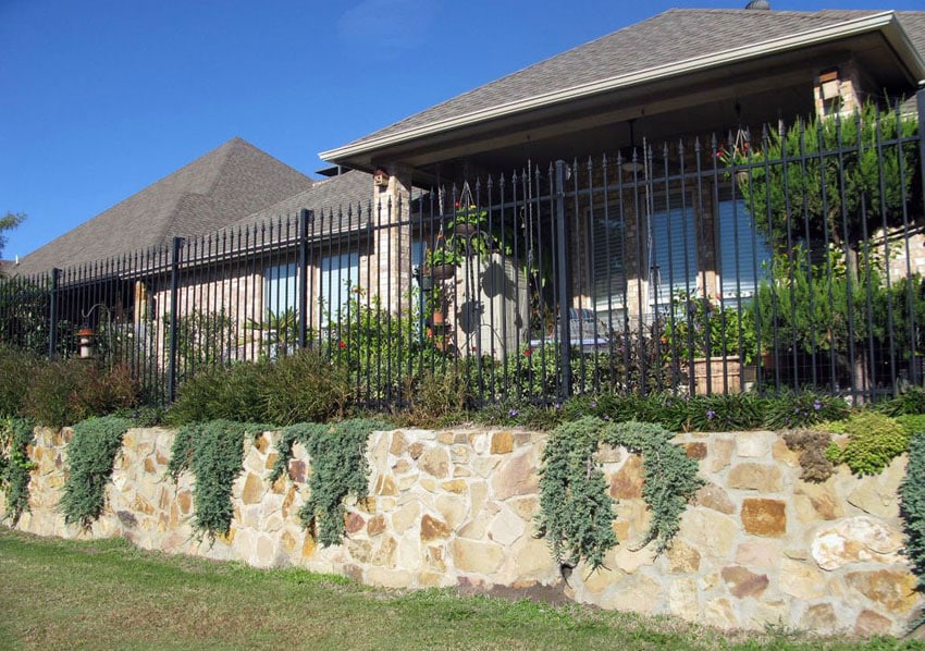 Black wrought iron fence and stone retaining wall
