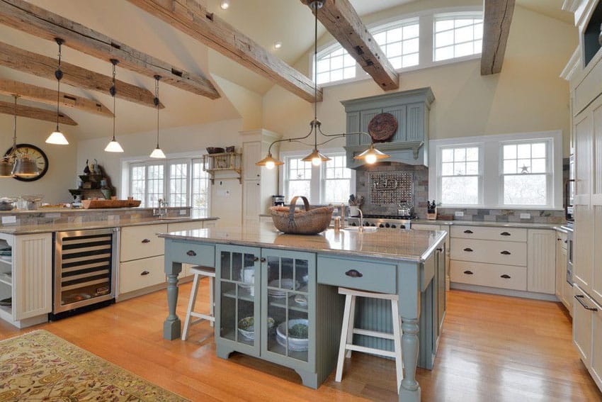 Country kitchen with exposed beams, white cabinets and painted island with blanco tulum granite counters