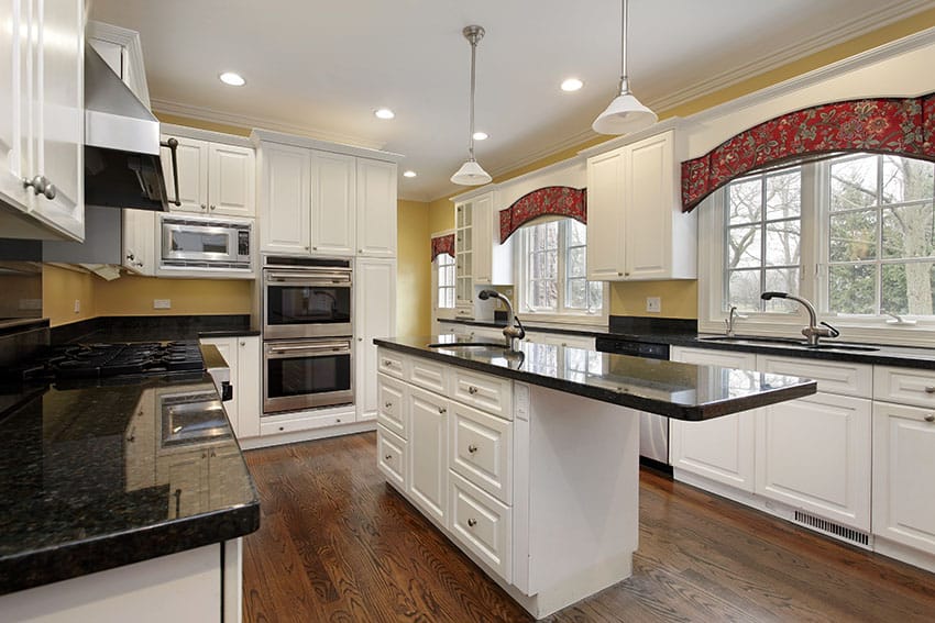 Country style kitchen design with white cabinets, black granite counters and island with overhanging counter