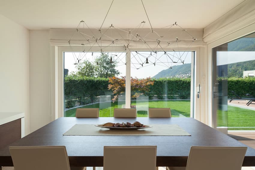 Room with modern art fixture, square table and a wide view of grassy lawn