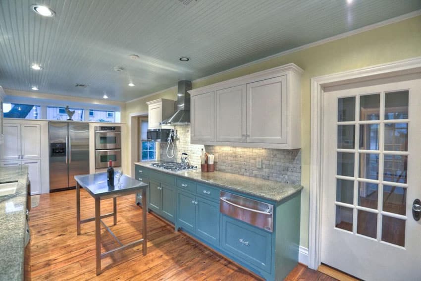 Kitchen space with blue bottom cabinets and white upper cabinets with portable metal island