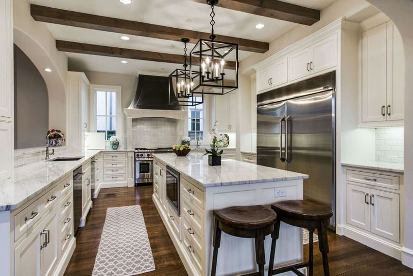 Luxury kitchen with white cabinets, oak wood floors, arabescato statuary marble counters and black wrought iron lamps