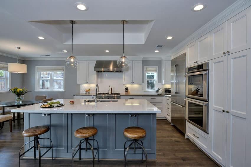 Kitchen with white shaker cabinets, blue island with white marble counters 