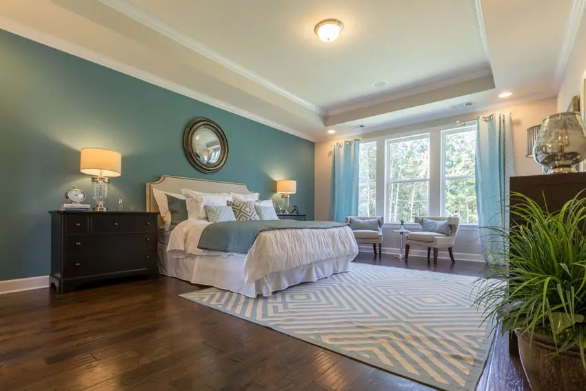 Luxury teal master bedroom with tray ceiling, wood floors and area rug