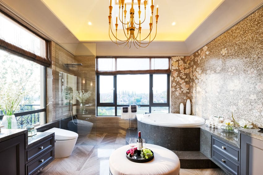Modern bathroom with large round tub, dark vanity, outdoor views and chandelier