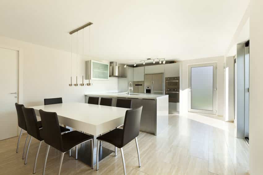 Modern dining table in open kitchen with white table, black chairs and chrome pendant lights
