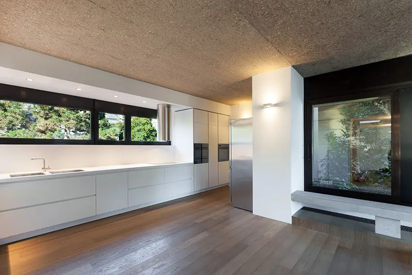 Modern galley kitchen with white cabinets, concrete ceilings, wood flooring and garden atrium views