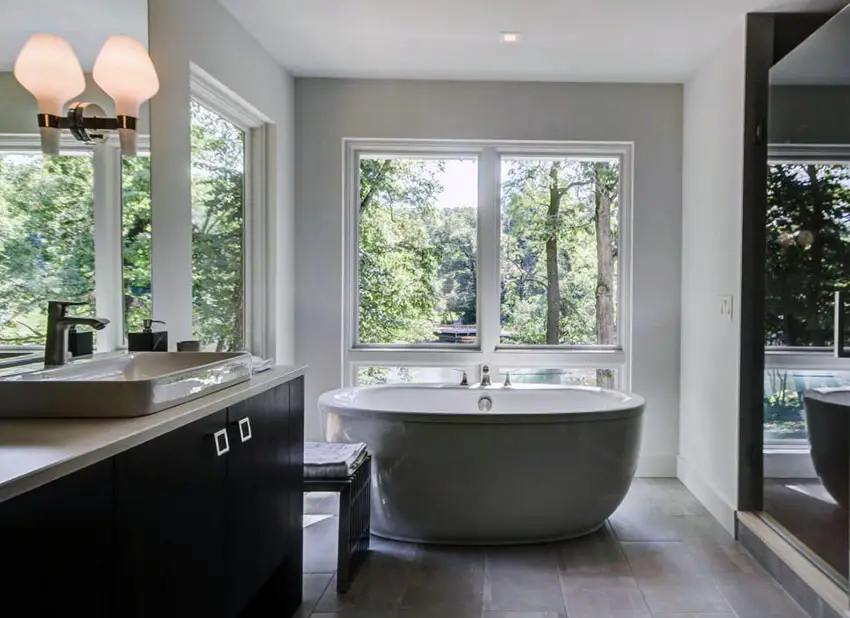 Modern master bathroom with bathtub window views, dark vanity and porcelain tile floors
