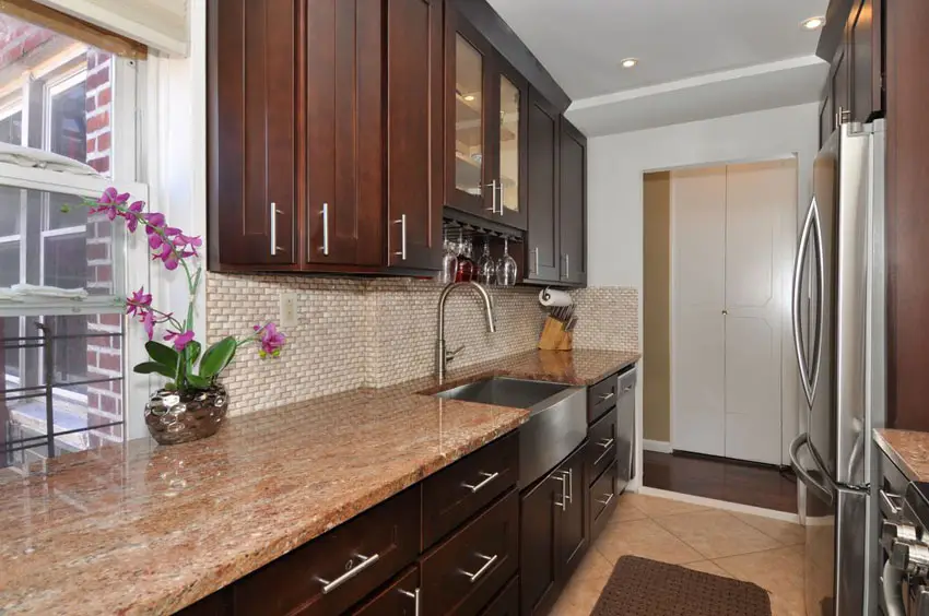 Narrow galley kitchen with brown cabinets and red astoria granite counter