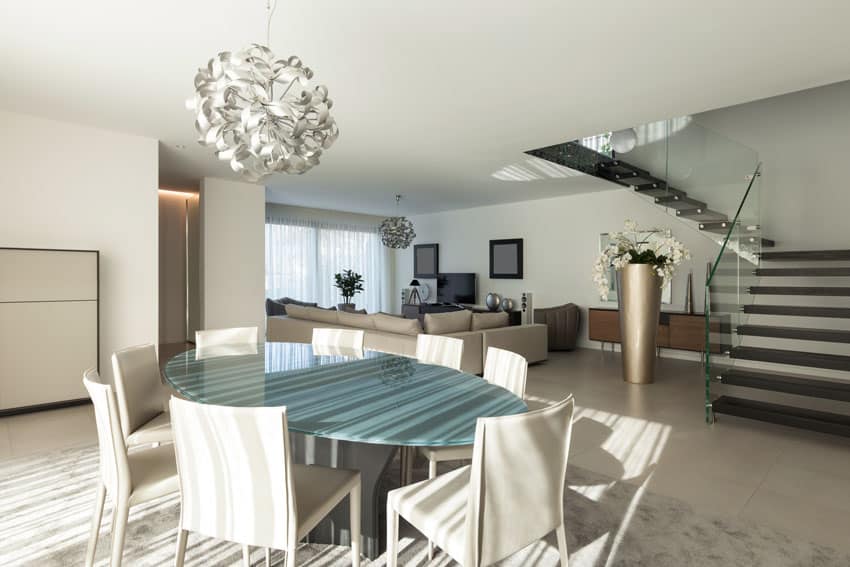 Oval table with green glass top, beige couches and large floor vase