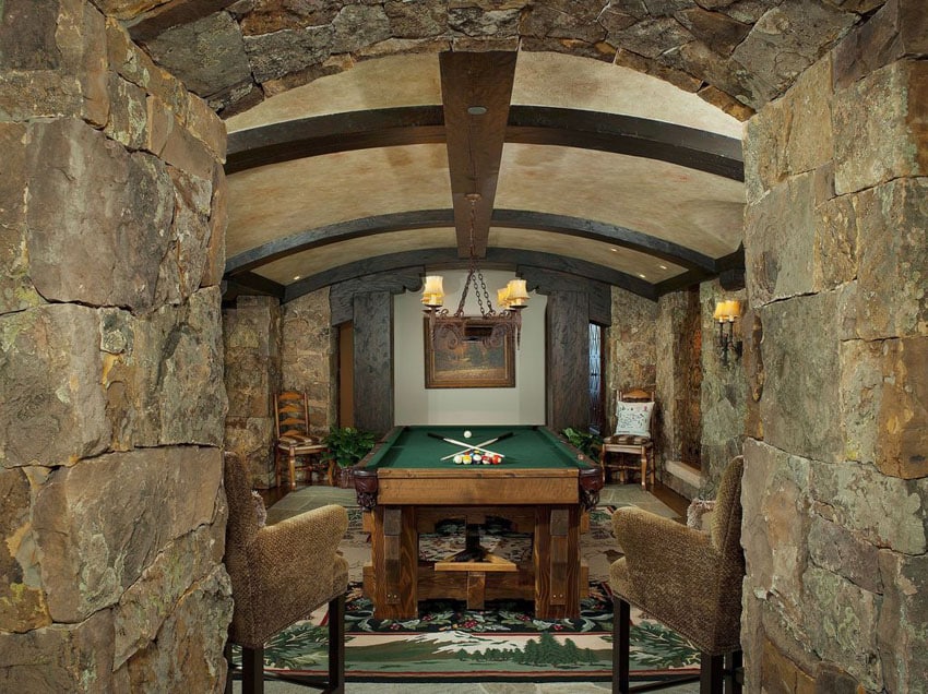 Rustic game room with stone walls arched ceiling and pool table