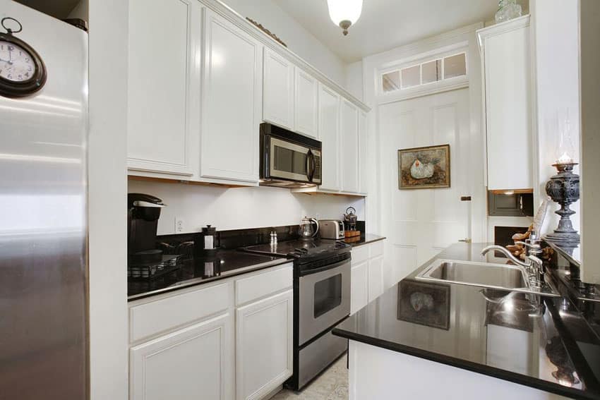 Small black and white galley kitchen with traditional white raised panel cabinets and black counters